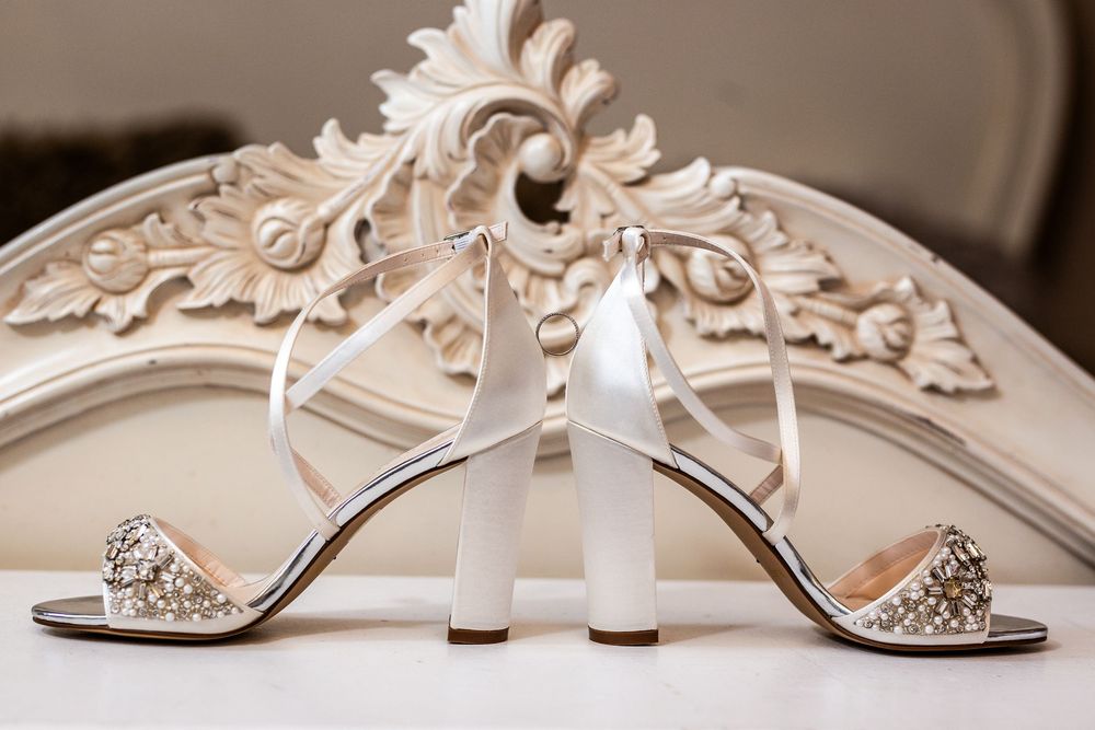 Elegant white satin bridal heels with crystal embellishments and ankle ties displayed against ornate carved decor.