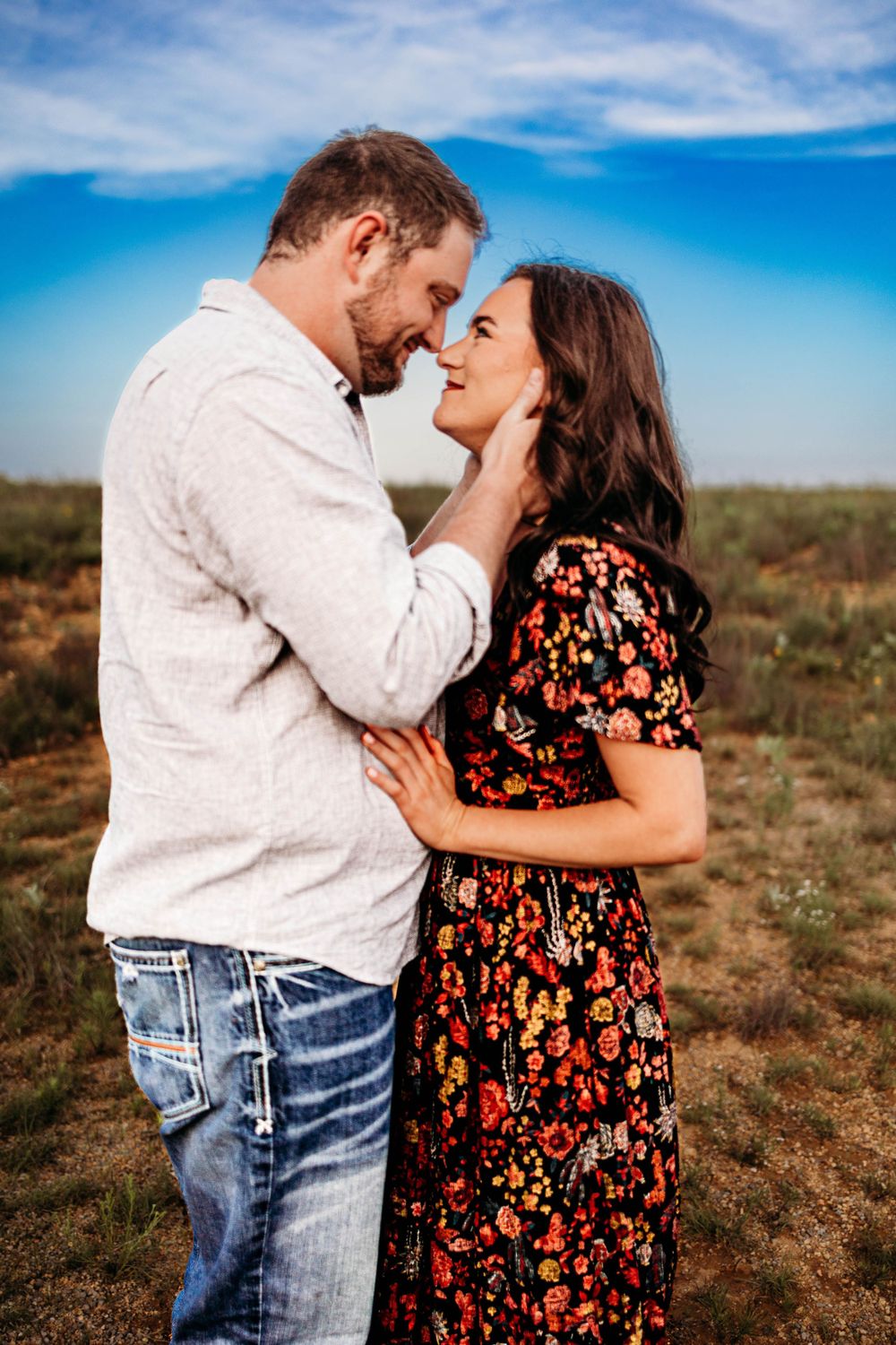 A romantic couple shares an intimate moment in a field against a bright blue sky on a sunny day.