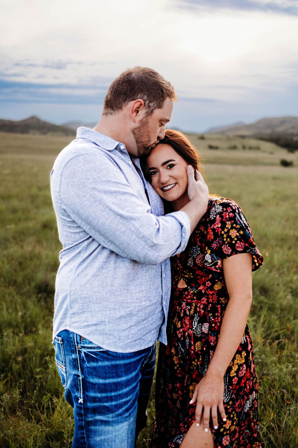 A gentle embrace photographed in a lush green field with mountains on the horizon.