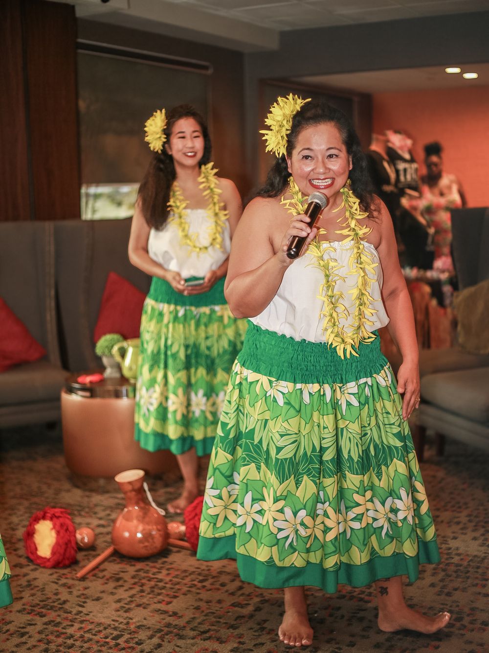 Hawaiian hula dancers in traditional green floral print dresses and yellow leis perform at a luau celebration.