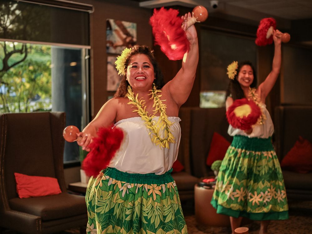 Traditional Hawaiian hula dancers wearing green skirts and yellow leis perform with red pom poms during a cultural show.