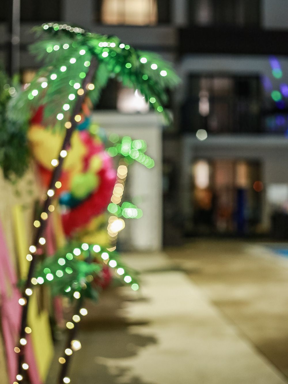 Illuminated palm tree decoration with green LED lights glows against a blurred urban background at night.