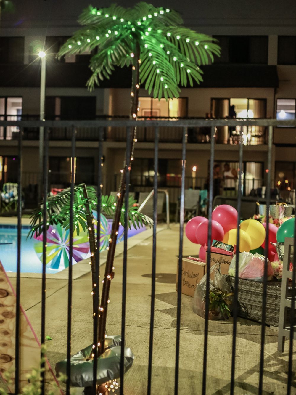 Decorative palm tree with LED lights and colorful balloons by a hotel pool at night.
