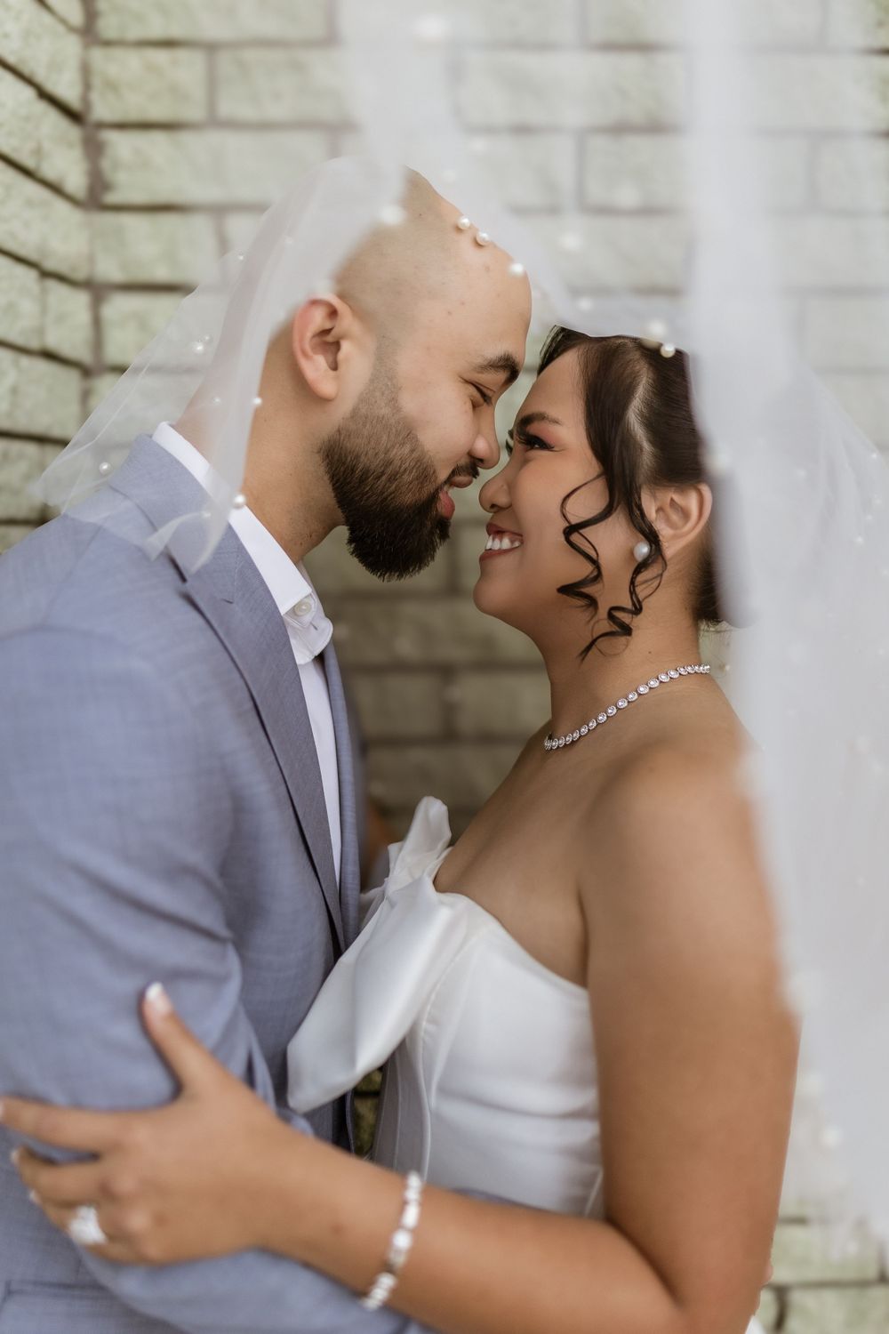 A tender moment between newlyweds against a white brick wall.