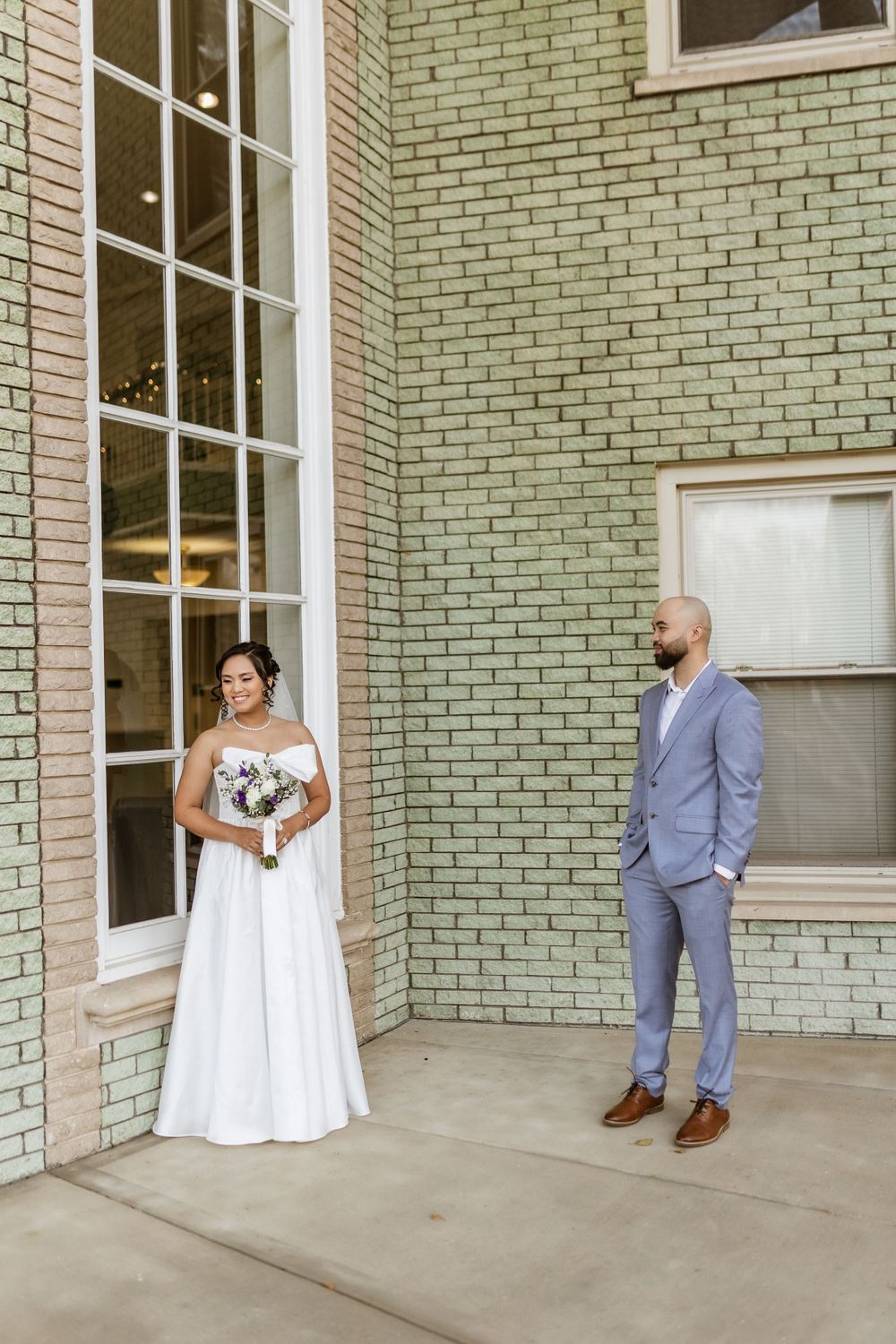 Wedding portrait with couple standing elegantly against mint green brick exterior.