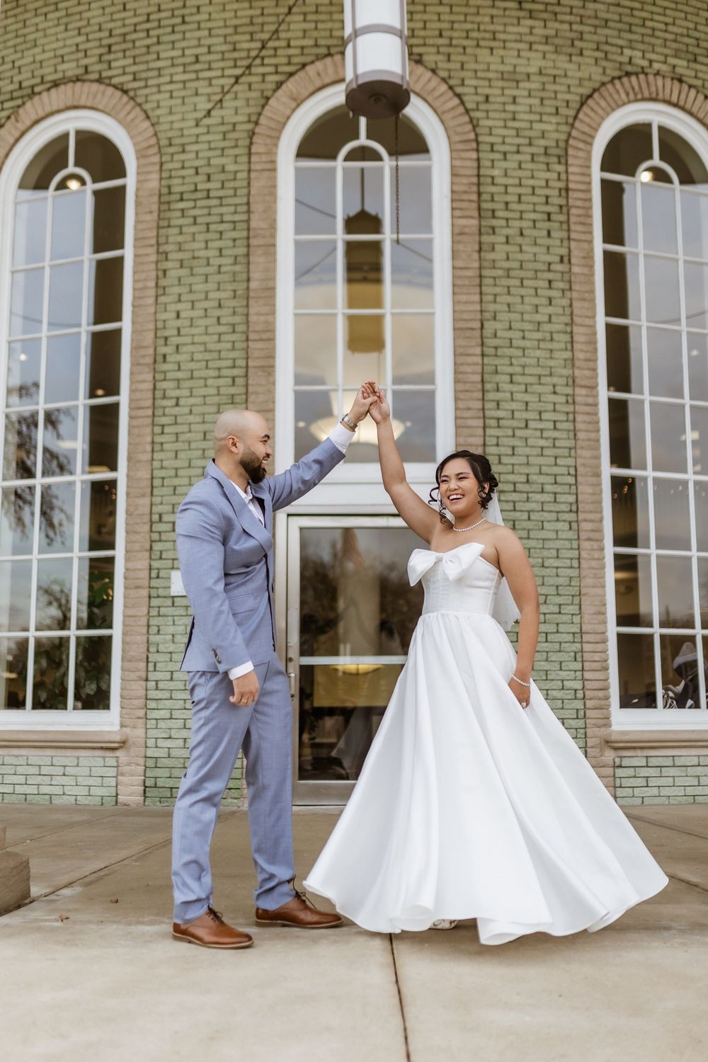 Joyful wedding celebration pose in front of historic building with arched windows.