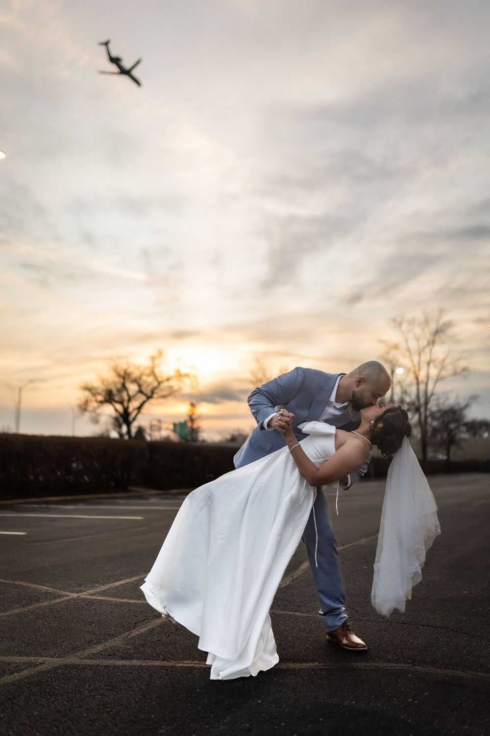 Romantic sunset wedding photo showing couple in dramatic dip pose against glowing sky and bare trees.