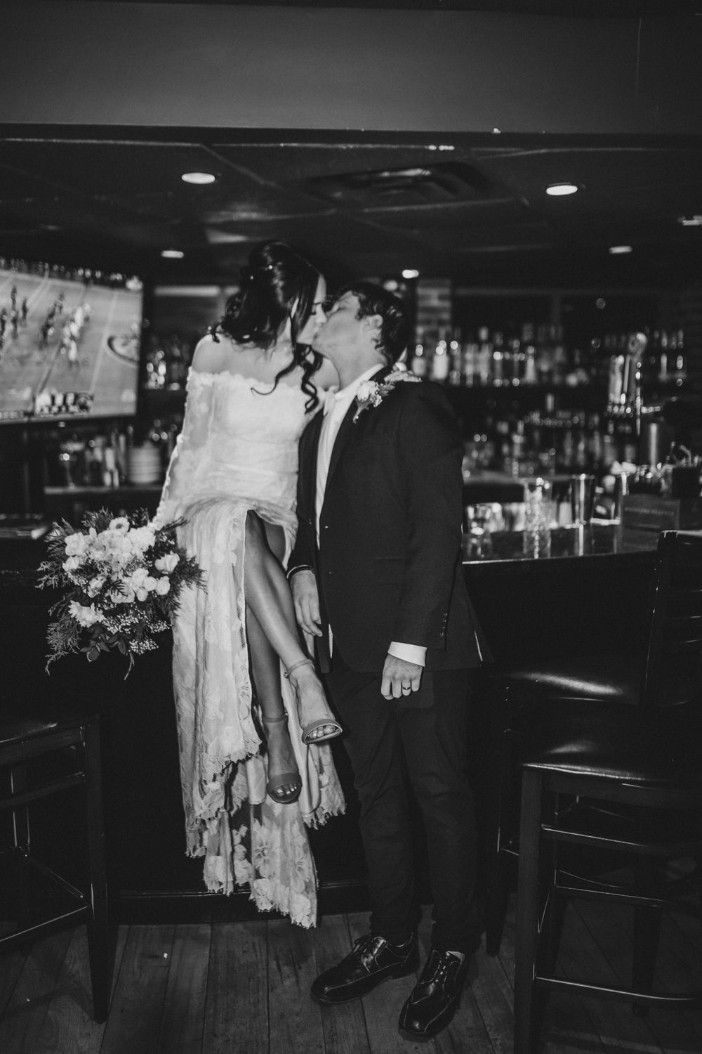 Black and white photo of couple sharing intimate moment at bar in vintage wedding attire.