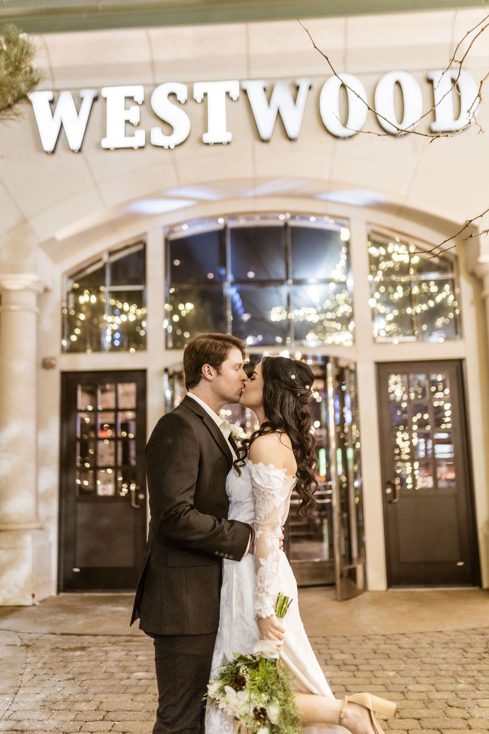 Couple sharing romantic moment outside Westwood venue with twinkling lights and elegant decor.