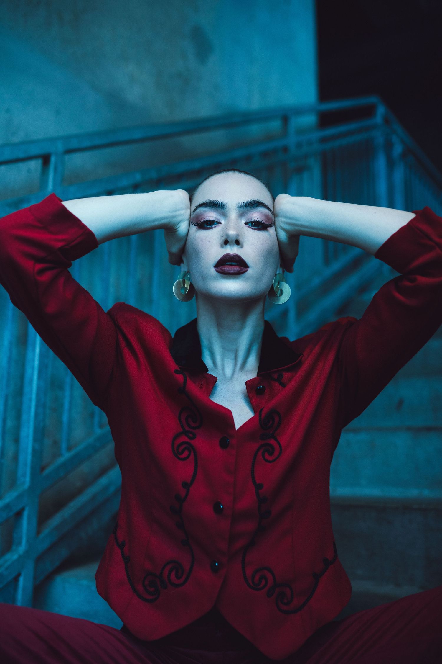 Dramatic portrait of figure in red jacket against moody blue background with artistic lighting.