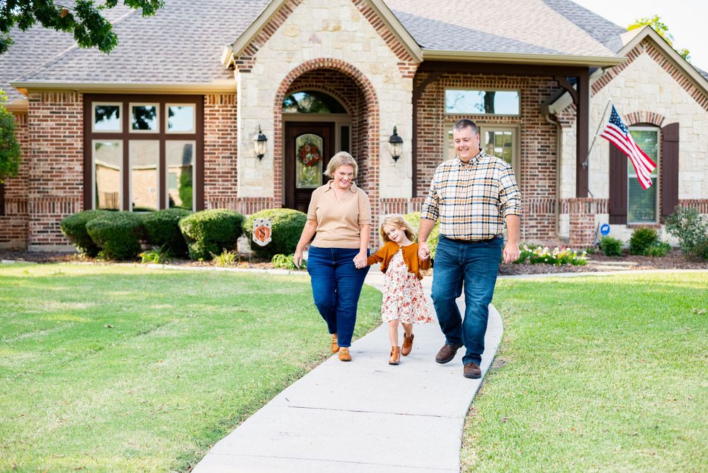 Family walking together on pathway leading to brick house with American flag.