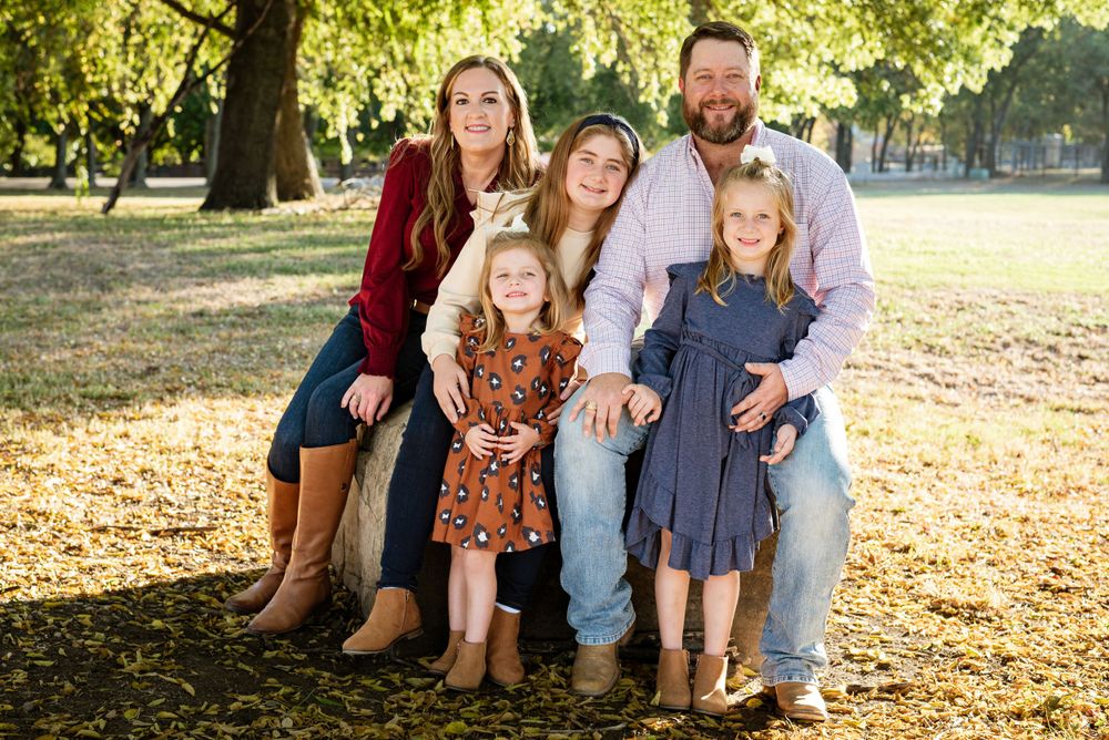 Family portrait taken in autumn park with golden sunlight filtering through trees.