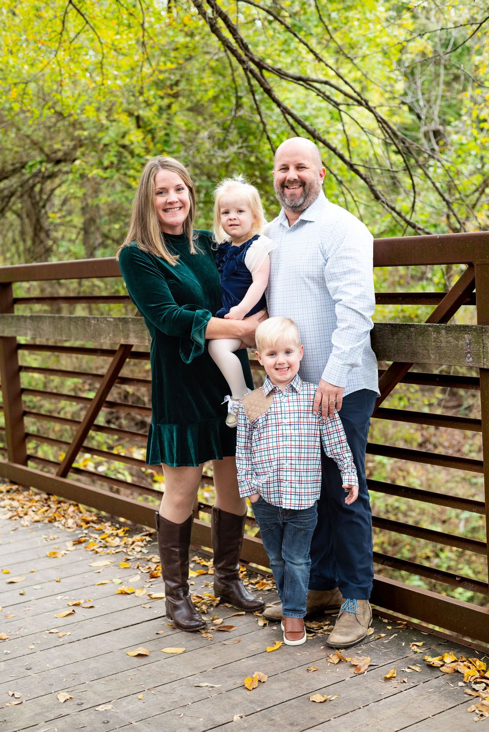 A family poses for a portrait on a wooden bridge surrounded by autumn foliage.