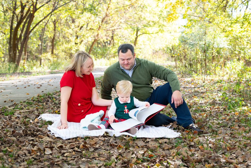 Family sitting on blanket surrounded by fall foliage in outdoor setting.