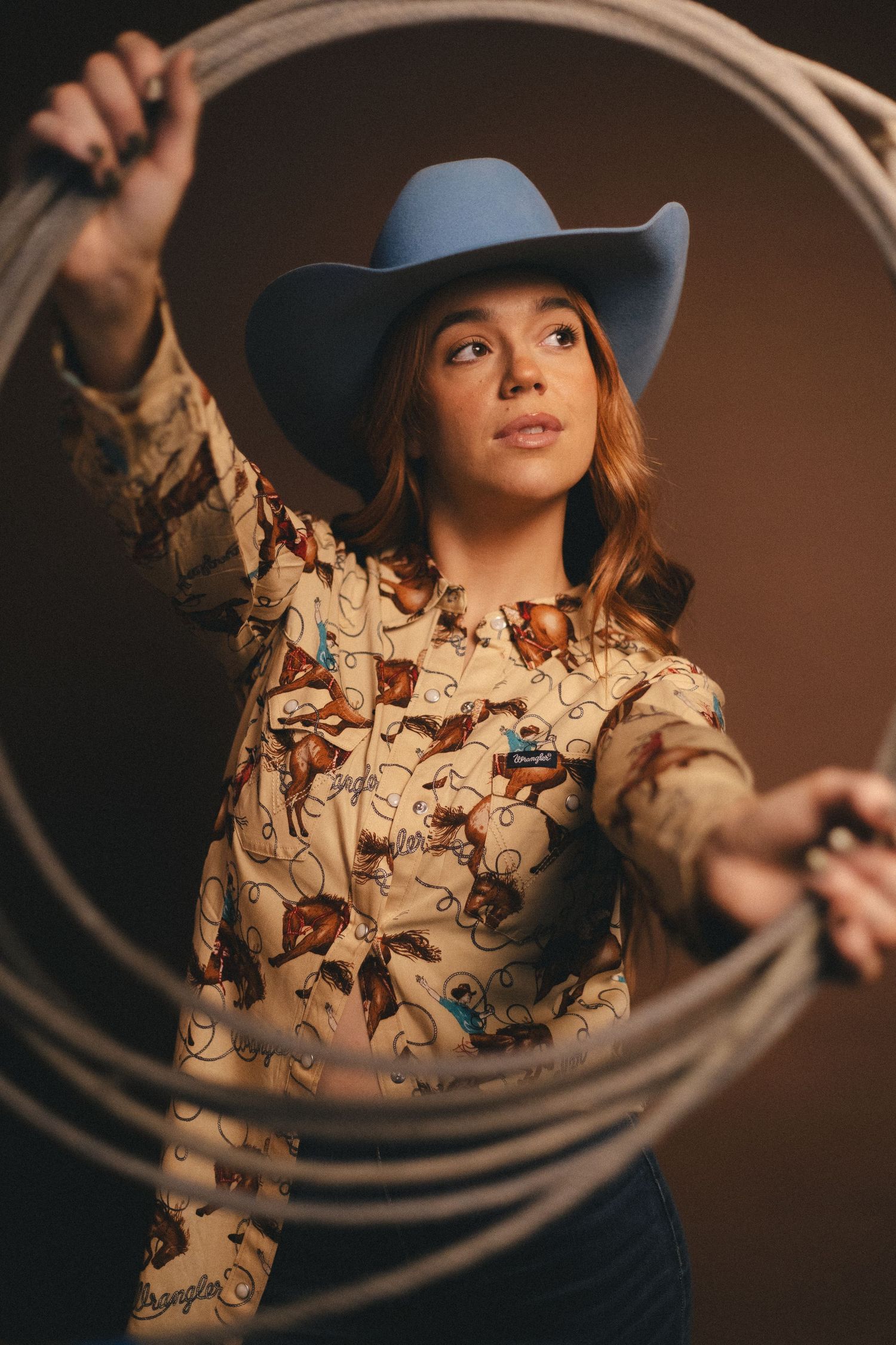 Western style portrait with floral shirt, blue cowboy hat and rope against dark background. Lake Geneva Wisconsin for Pro-Hats