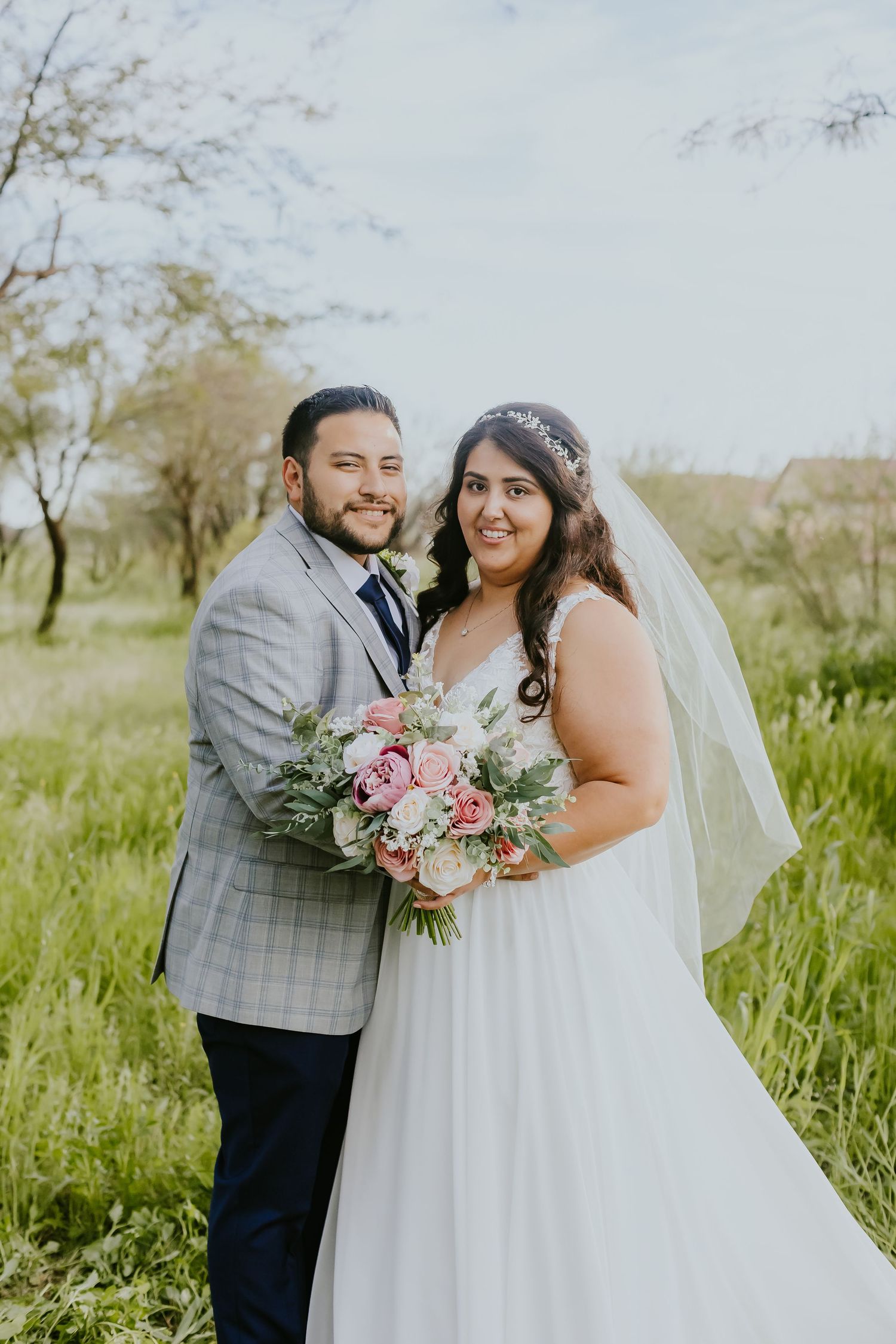 Spring wedding portraits in lush green field with pink floral bouquet.