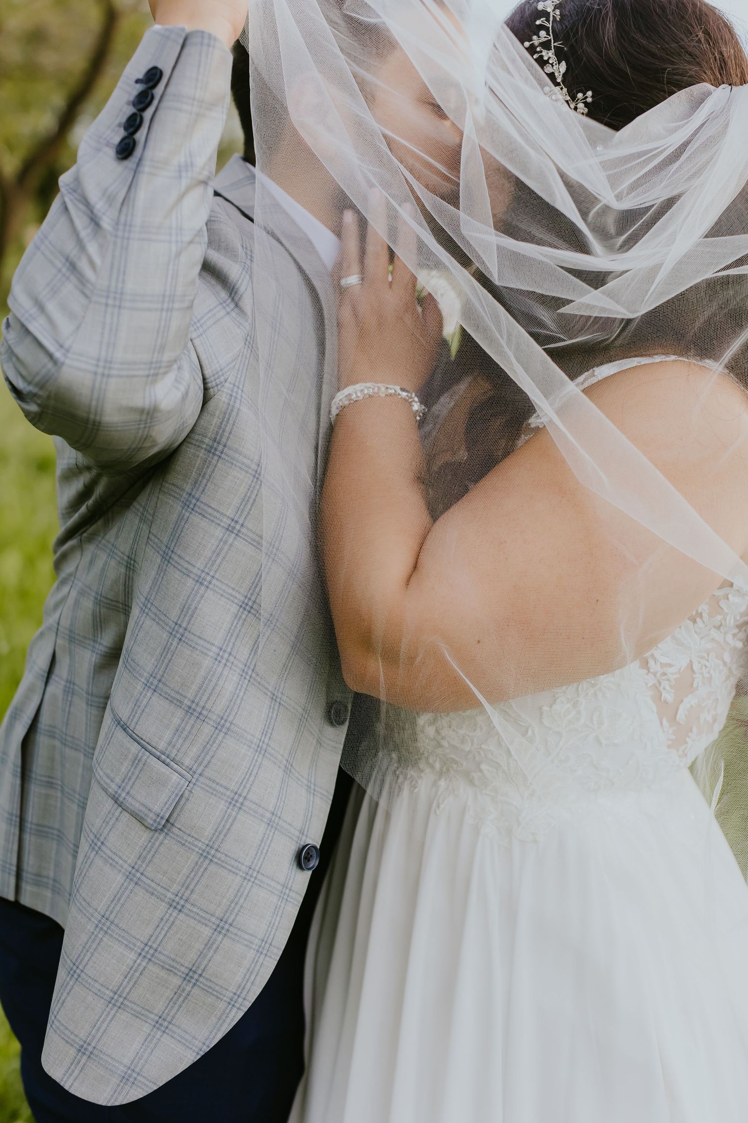 Close-up detail of a bride's veil and groom's gray checkered suit jacket during an outdoor wedding.