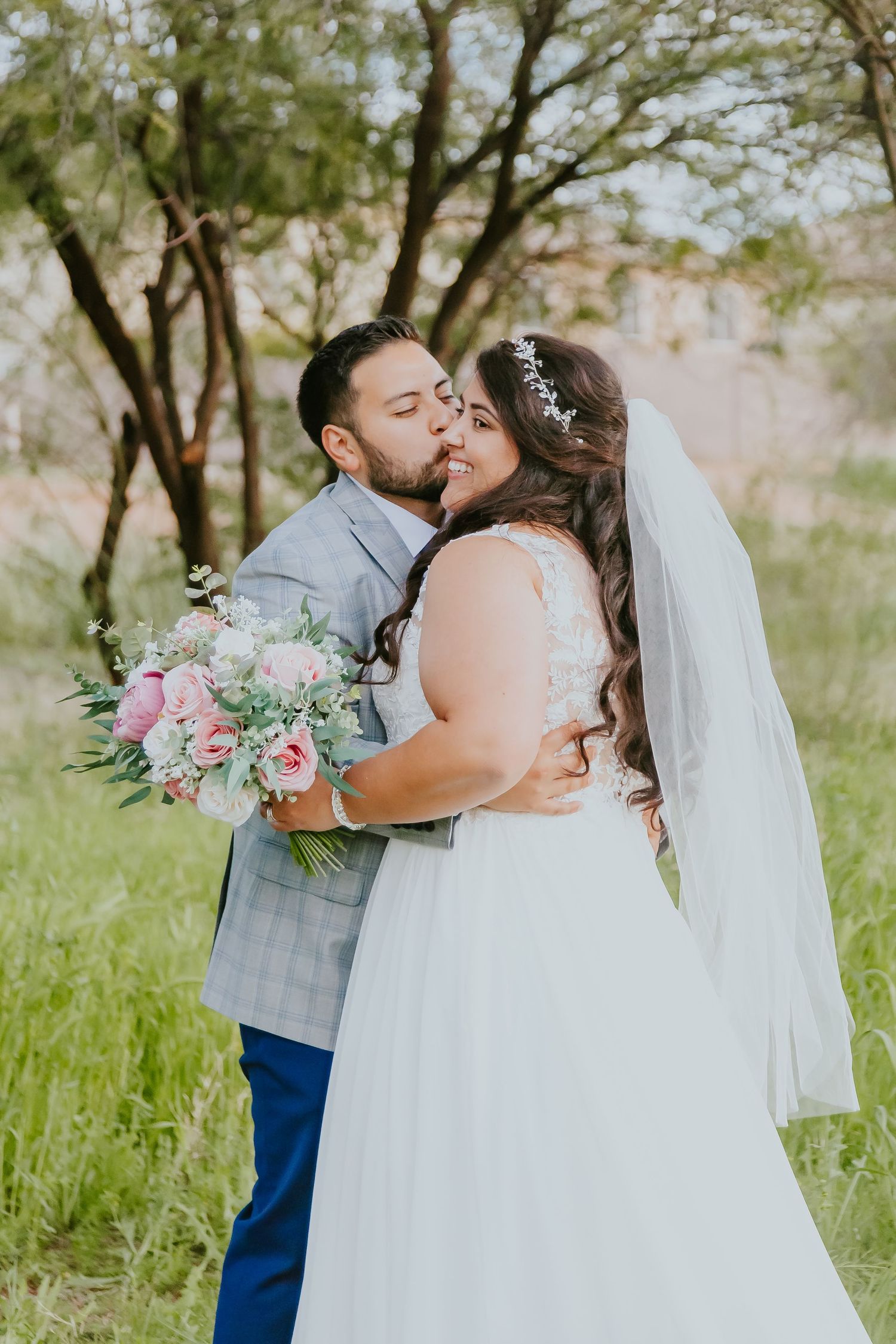 Romantic wedding portraits in green spring meadow with flowing white dress and pink bouquet.