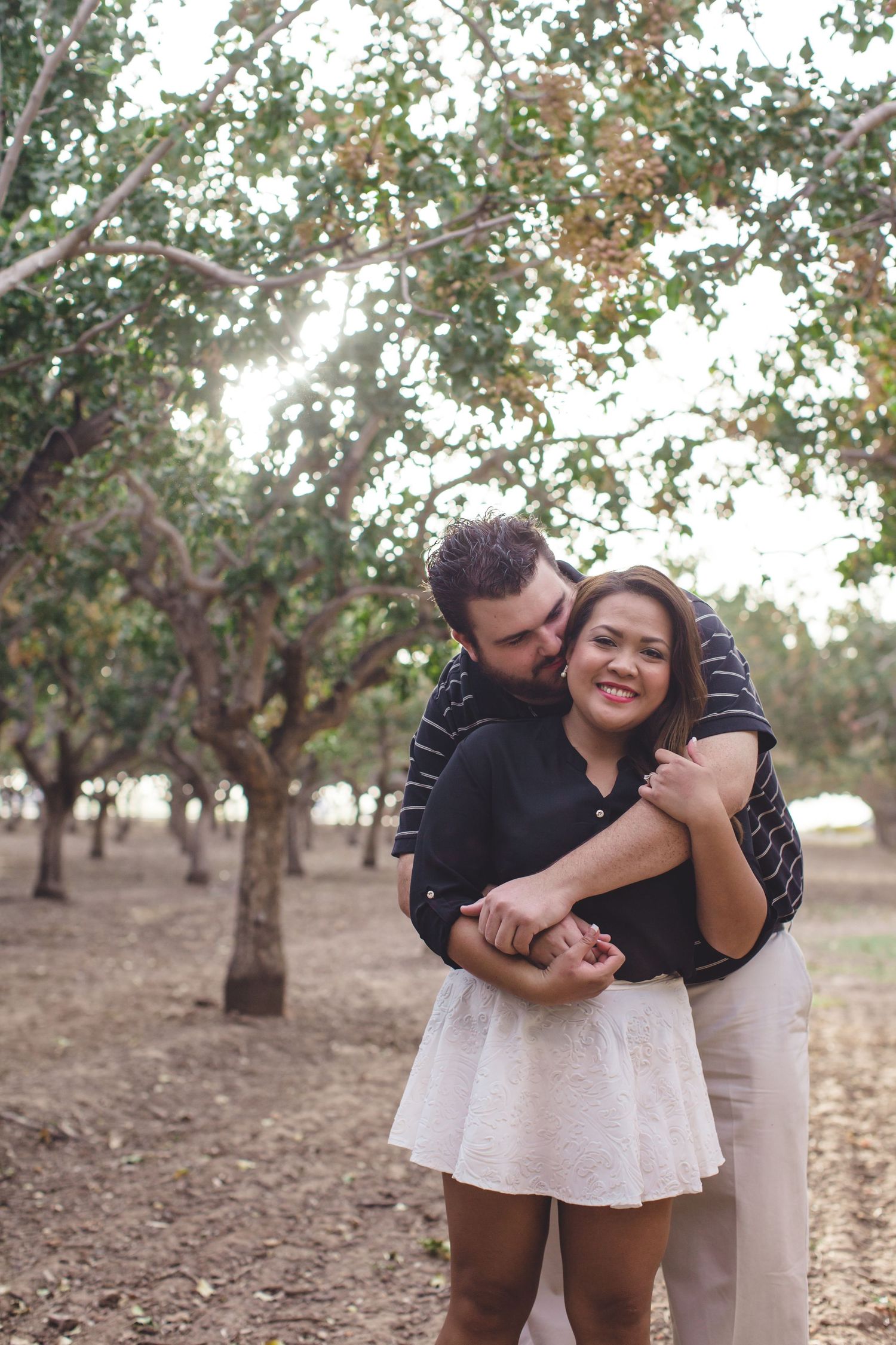 Playful couple photoshoot in orchard with natural lighting and trees.