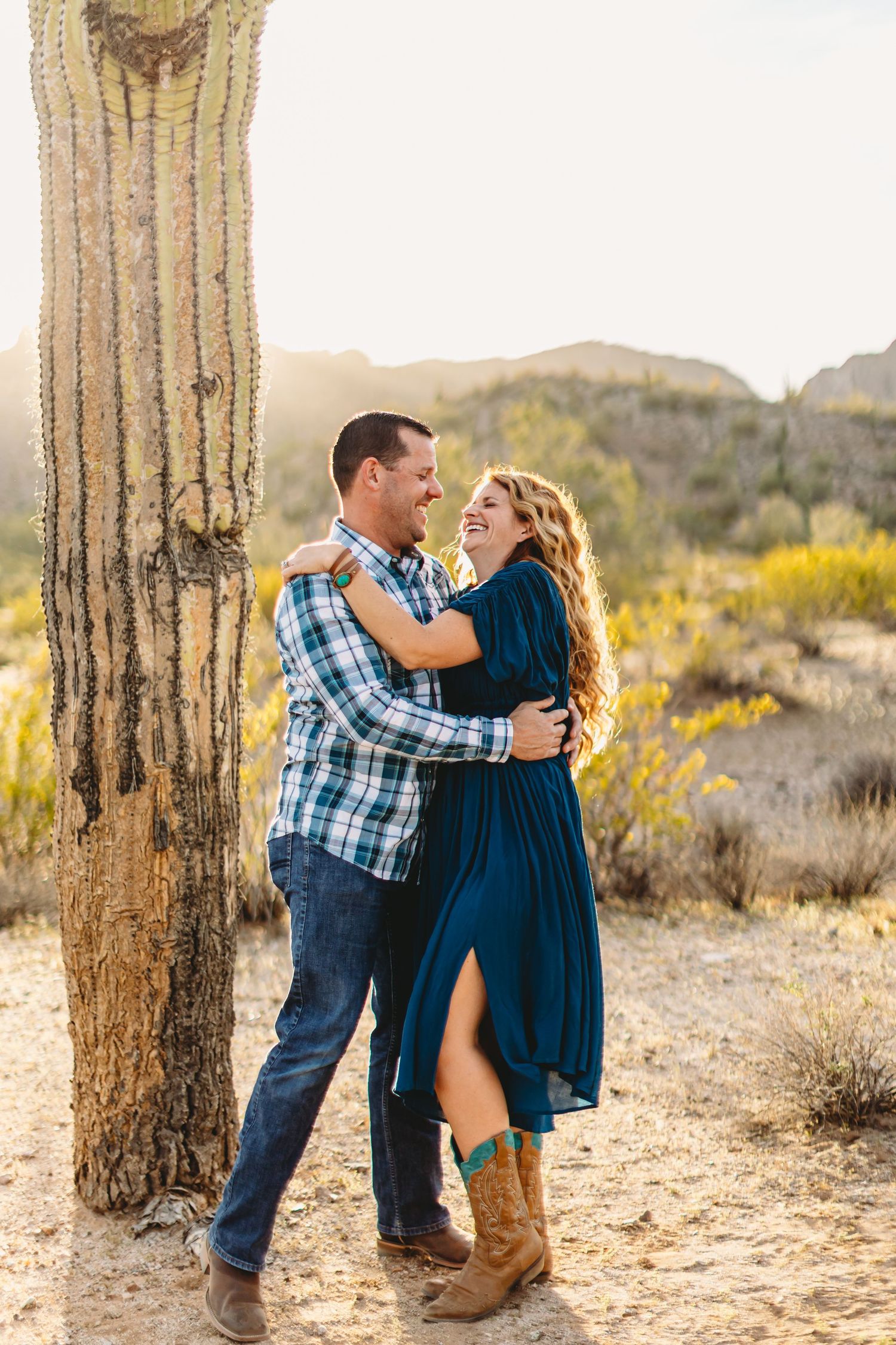 Desert engagement photos with couple embracing near majestic saguaro cactus.