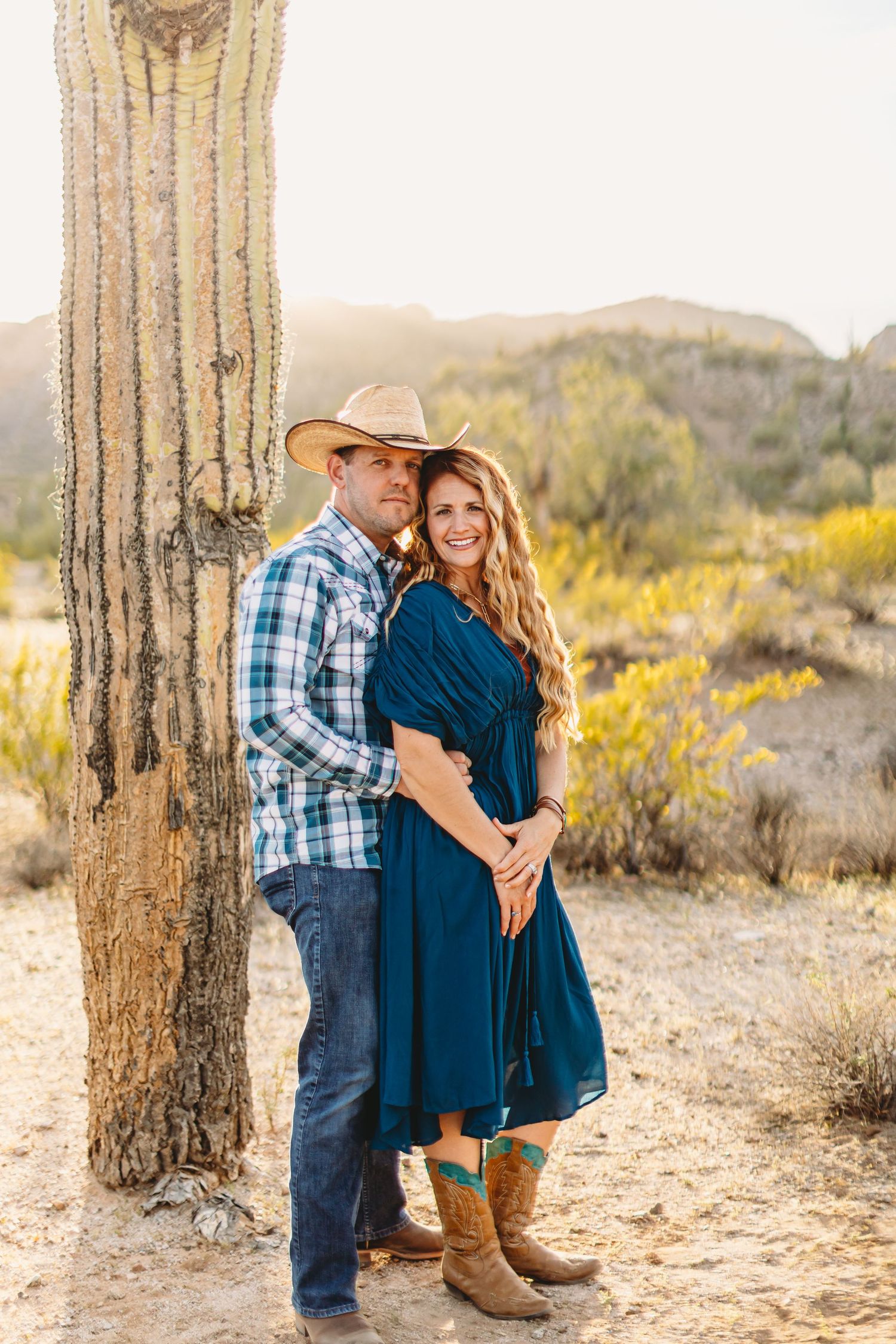Desert engagement session with couple in blue outfits against saguaro cactus backdrop.