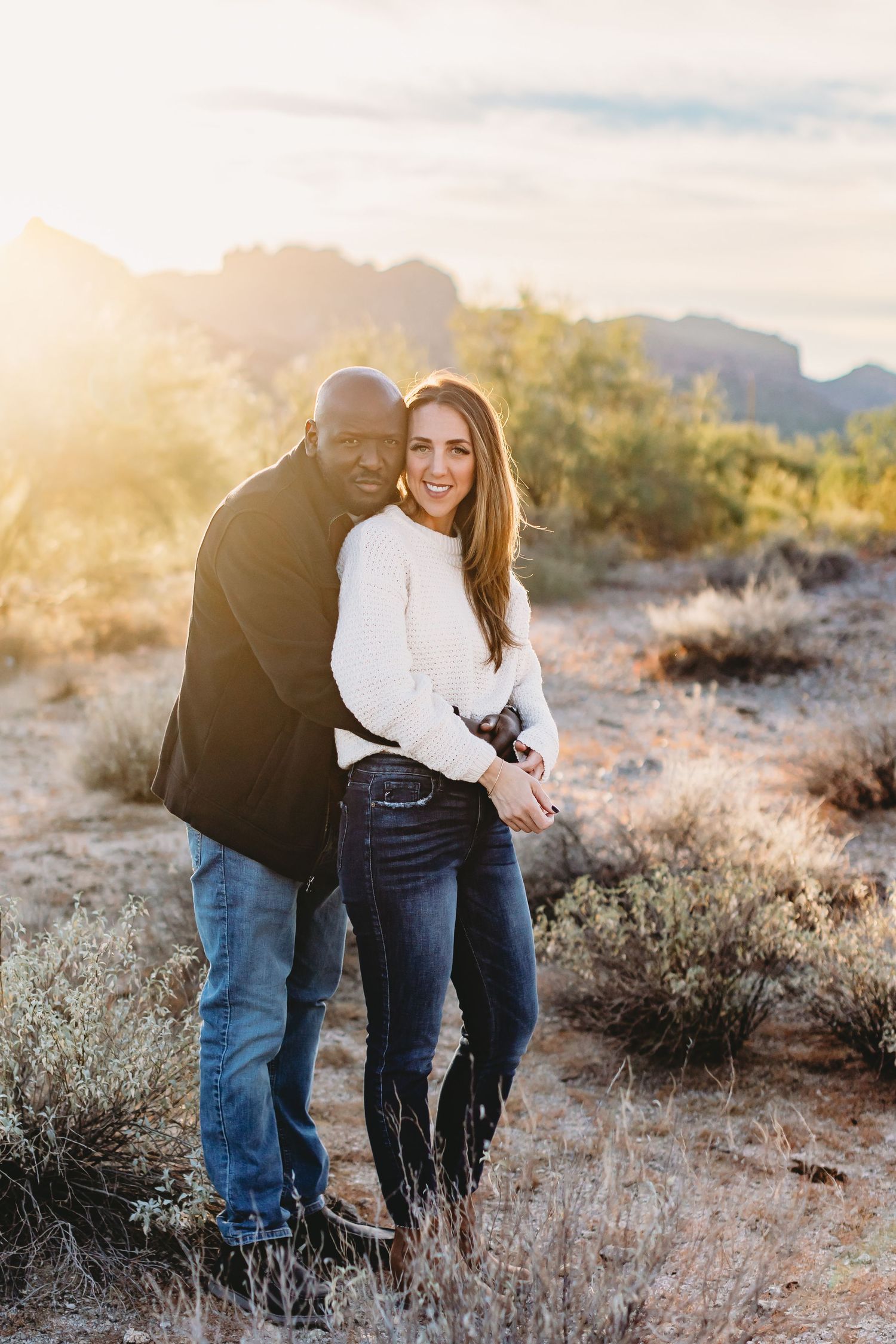Intimate portrait of couple in casual wear against desert mountain backdrop at sunset.