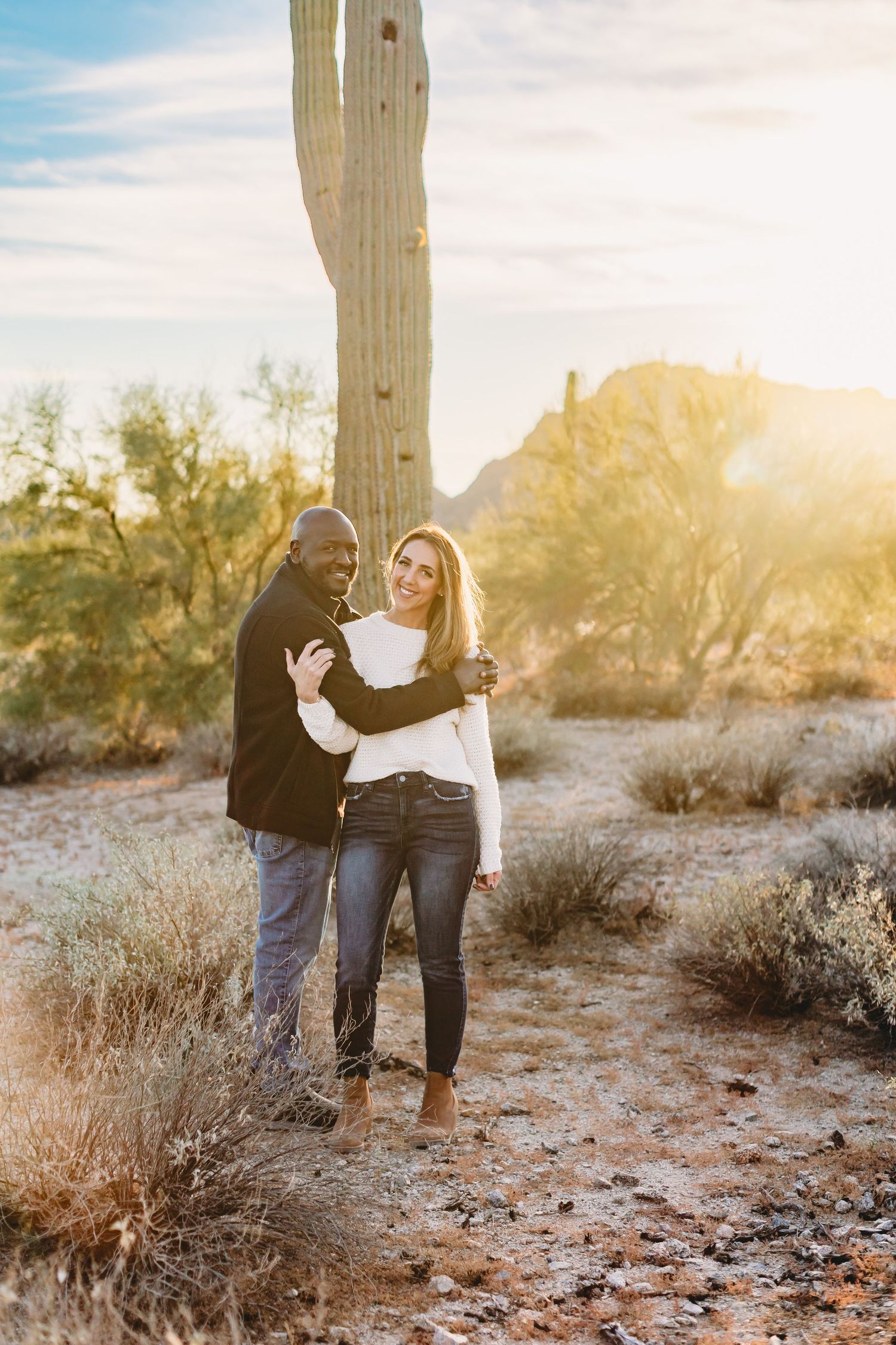 Couple sharing tender moment near tall saguaro cactus during desert sunset.