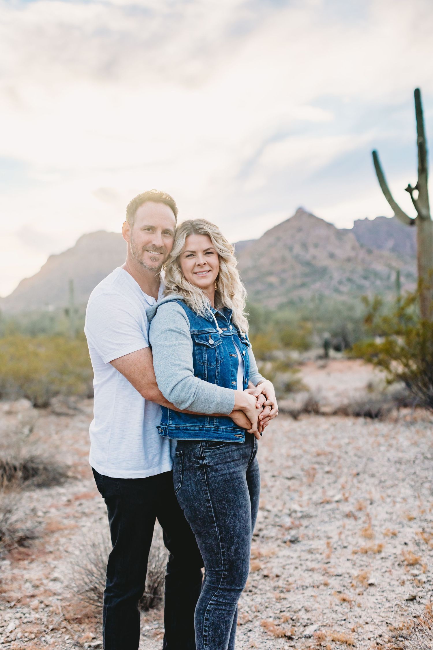 Happy couple in casual wear embracing against desert mountain backdrop.