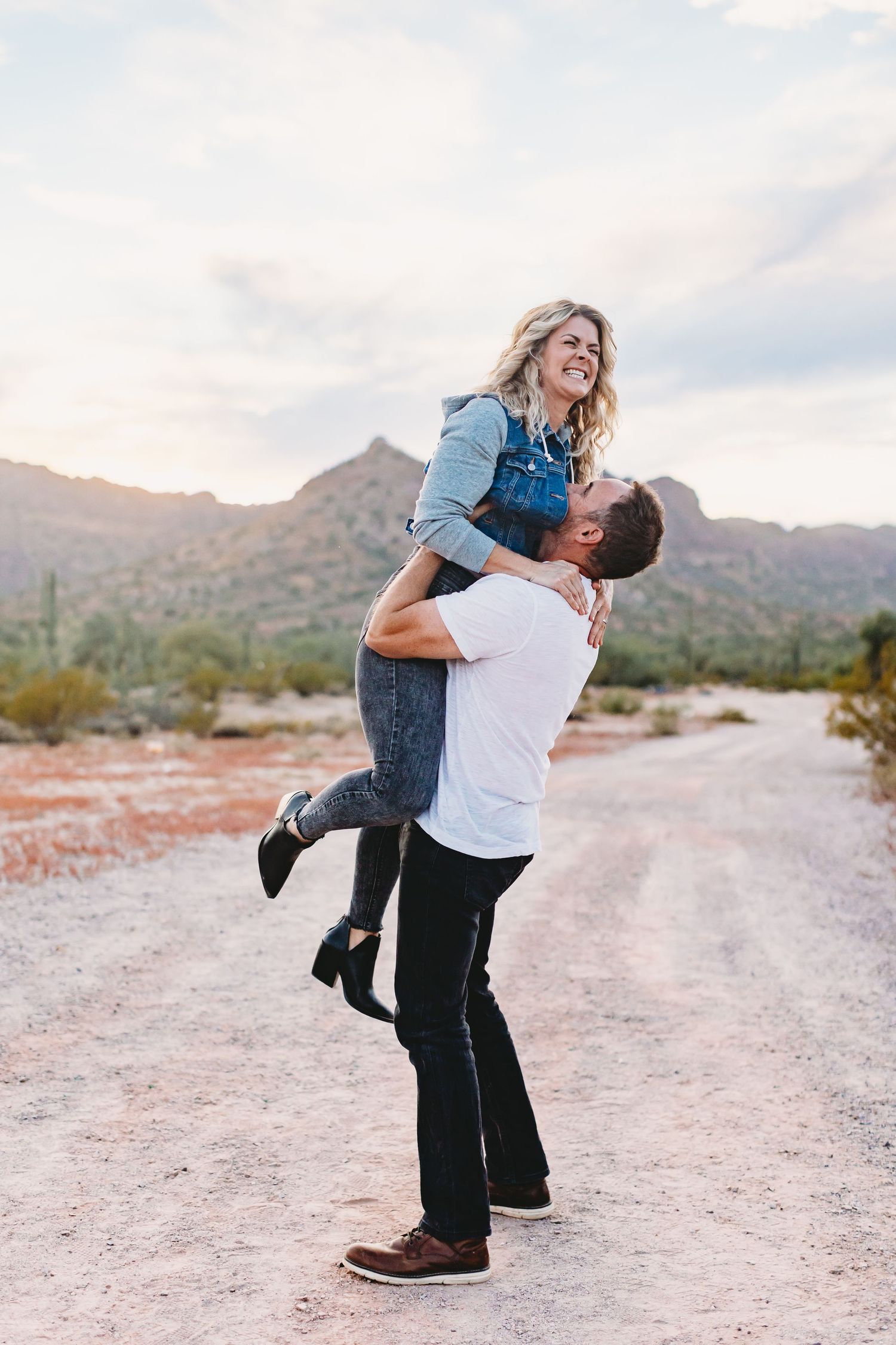 A couple shares a joyful spinning moment on a desert path with mountains in the background.