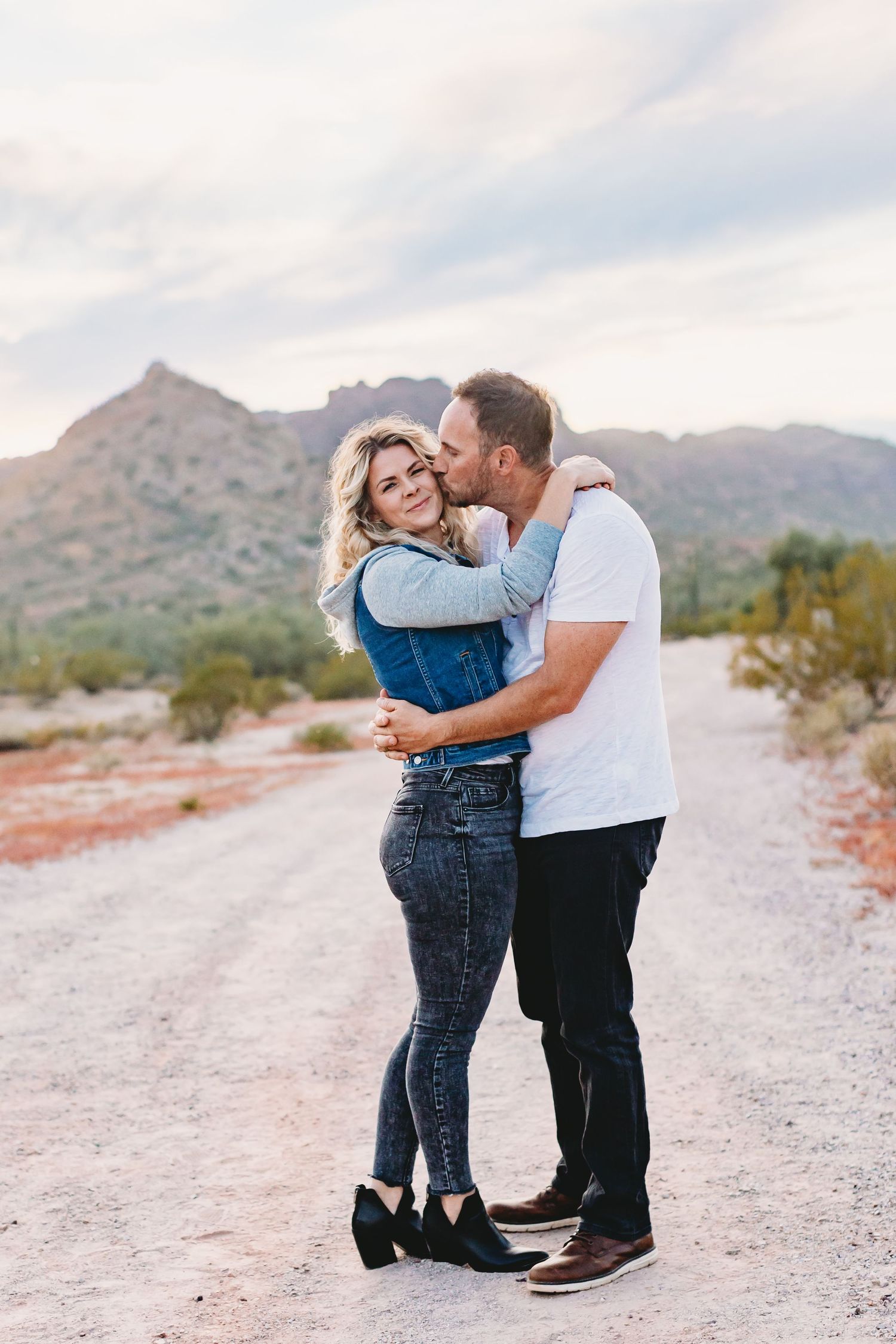 A romantic couple moment captured on a desert path with mountain views at sunset.