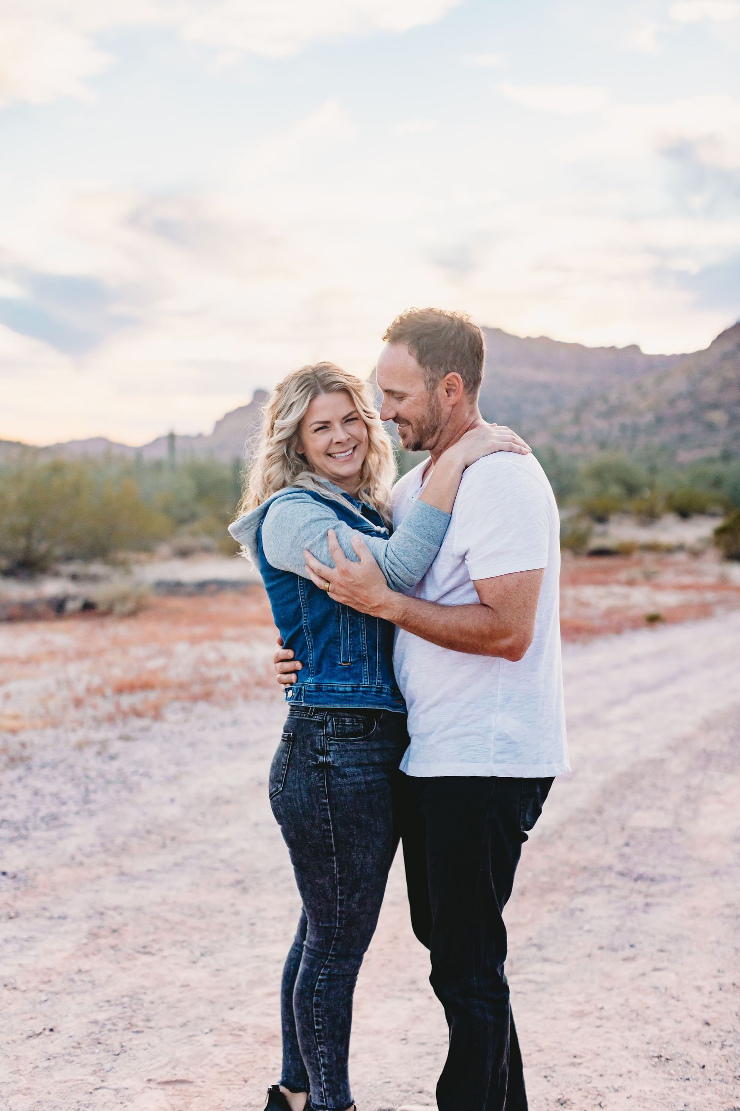 A couple shares an intimate moment on a desert trail with mountains in the background.