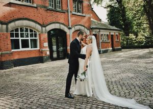 Bride and groom share a romantic moment on cobblestone courtyard outside a red brick building on their wedding day.