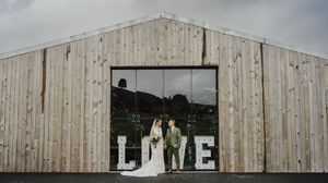 A large wooden barn wedding venue with white LOVE letters displayed in the open doorway.