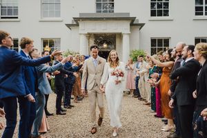 Wedding guests line up on gravel path outside historic building to celebrate with bubbles and confetti.