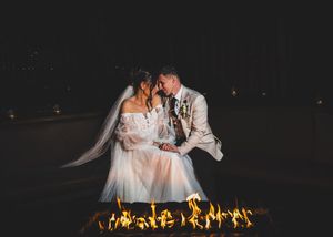 A romantic couple shares an intimate moment in front of a glowing fire feature at night.