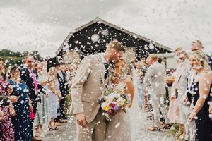 Wedding guests shower newlyweds with flower petals and confetti as they walk through a joyful celebration line outdoors.