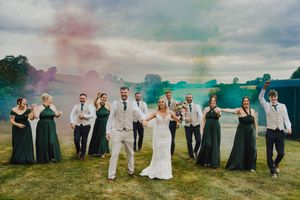 Wedding party dressed in formal attire poses in silhouette against dramatic cloudy sky on rolling green hillside.