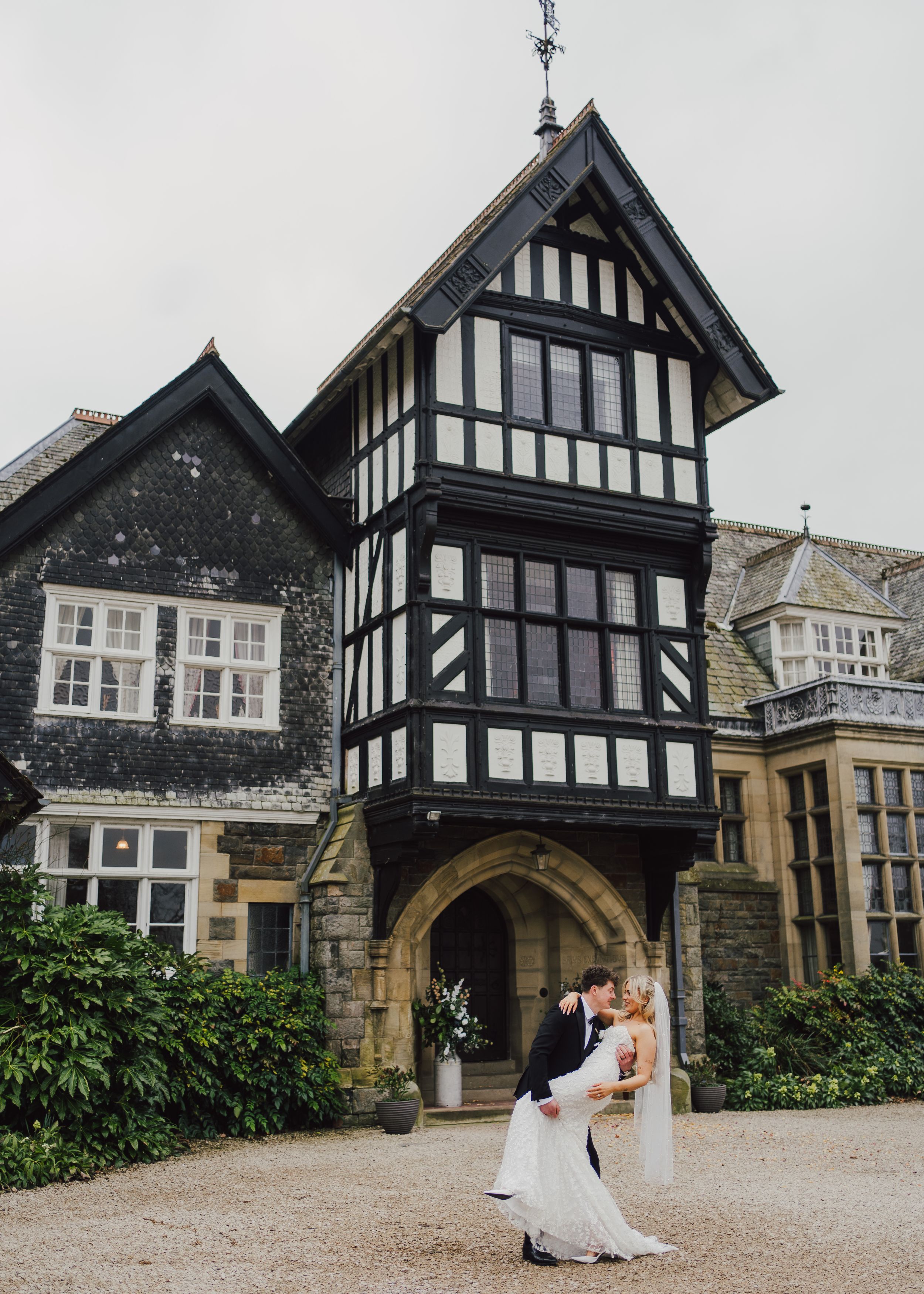 Elegant Tudor-style manor house with black and white timber framing features a romantic archway entrance on overcast day.