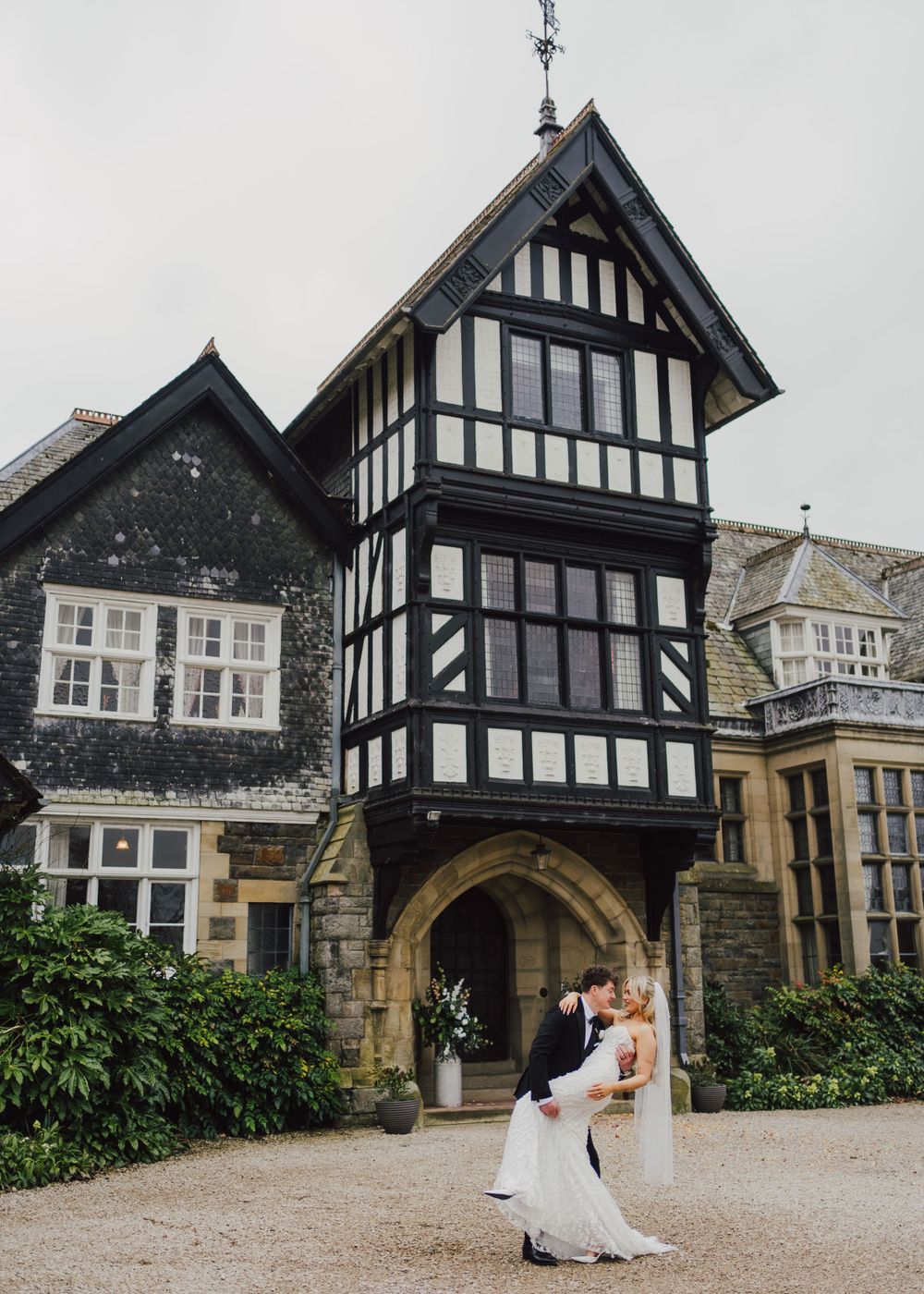 Elegant Tudor-style manor house with black and white timber framing features a romantic archway entrance on overcast day.