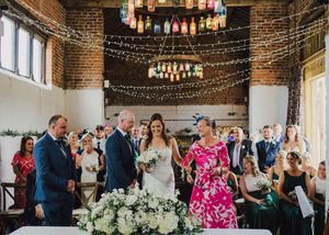 Wedding ceremony in a rustic brick venue decorated with string lights and floral arrangements.