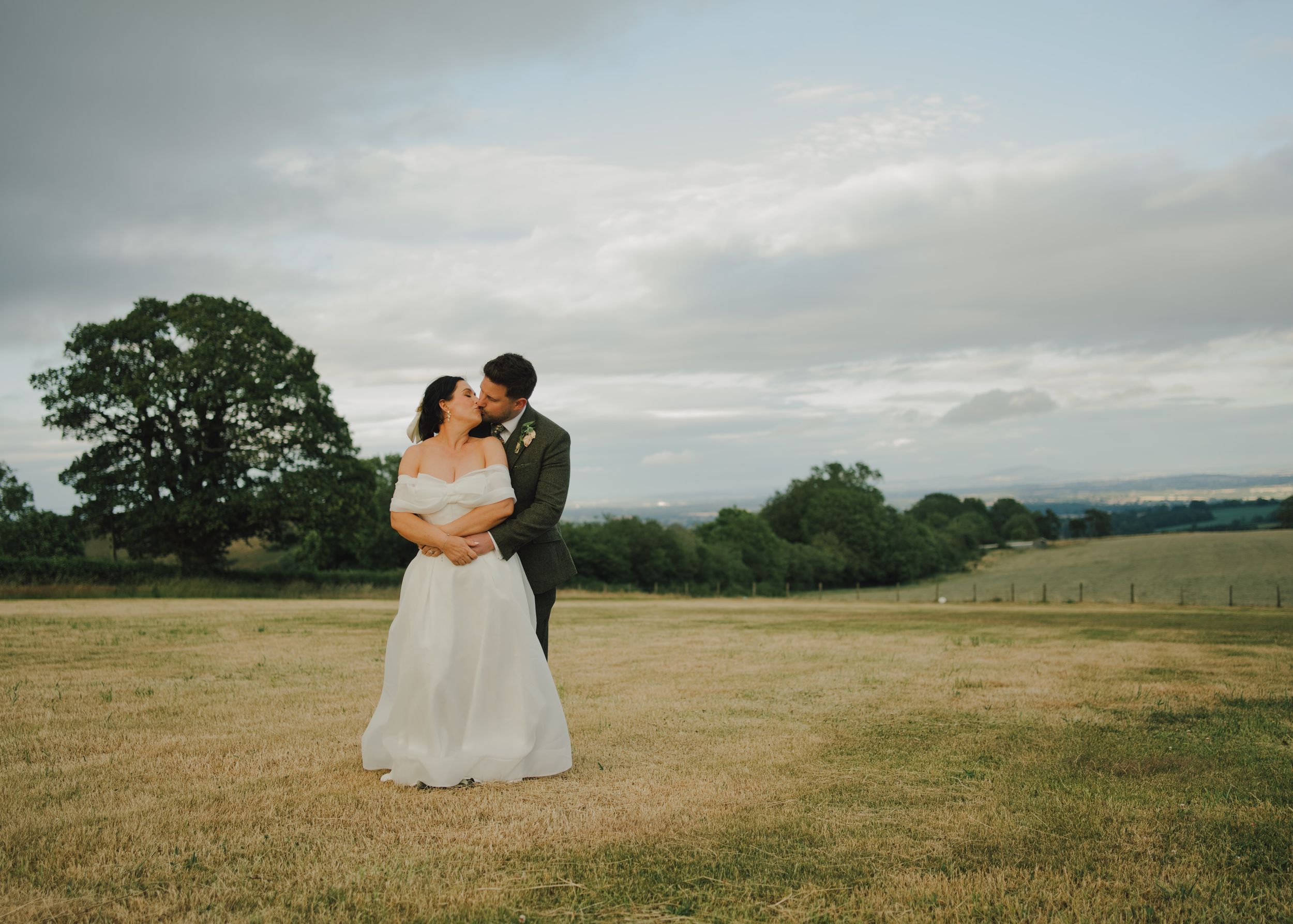 Bride and groom share a romantic moment in a lush green countryside field on their wedding day.