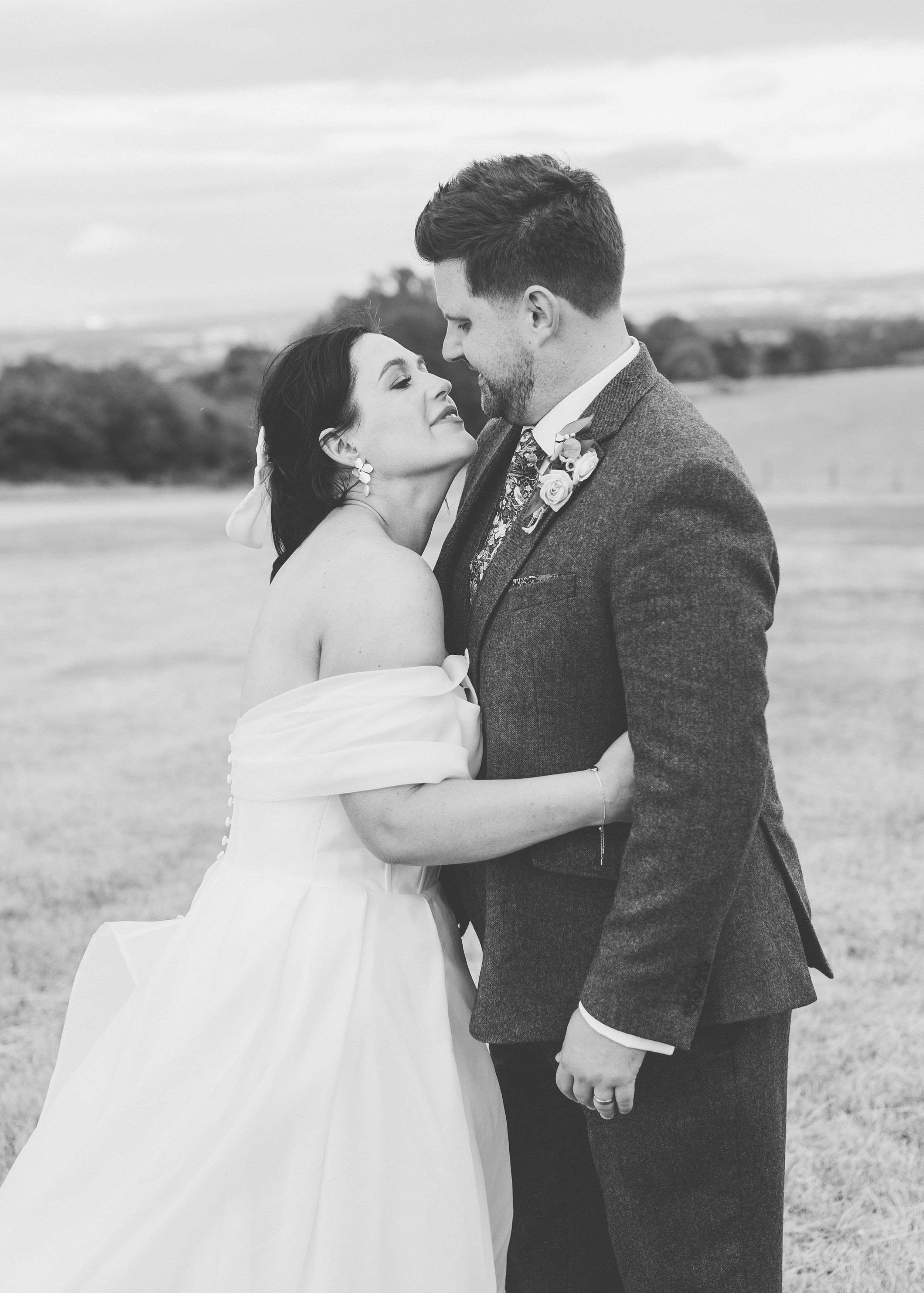 Black and white photo of a bride and groom sharing a romantic moment in an open field on their wedding day.