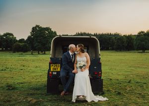 People sit outdoors in formal attire surrounded by lush green meadows during sunset.