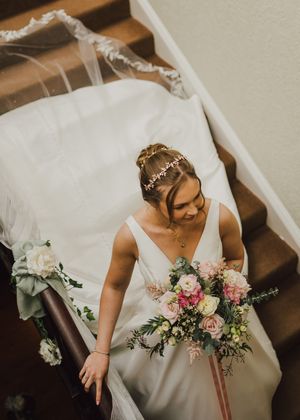 A bride in a white gown joyfully reaches for her wedding bouquet filled with pink and blush roses.