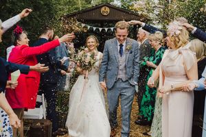 Guests throw confetti during an outdoor wedding celebration as newlyweds celebrate beneath trees and festive decorations.
