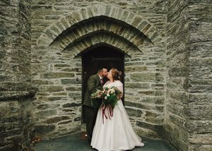 Bride and groom kissing under a stone archway at a rustic castle wedding venue.
