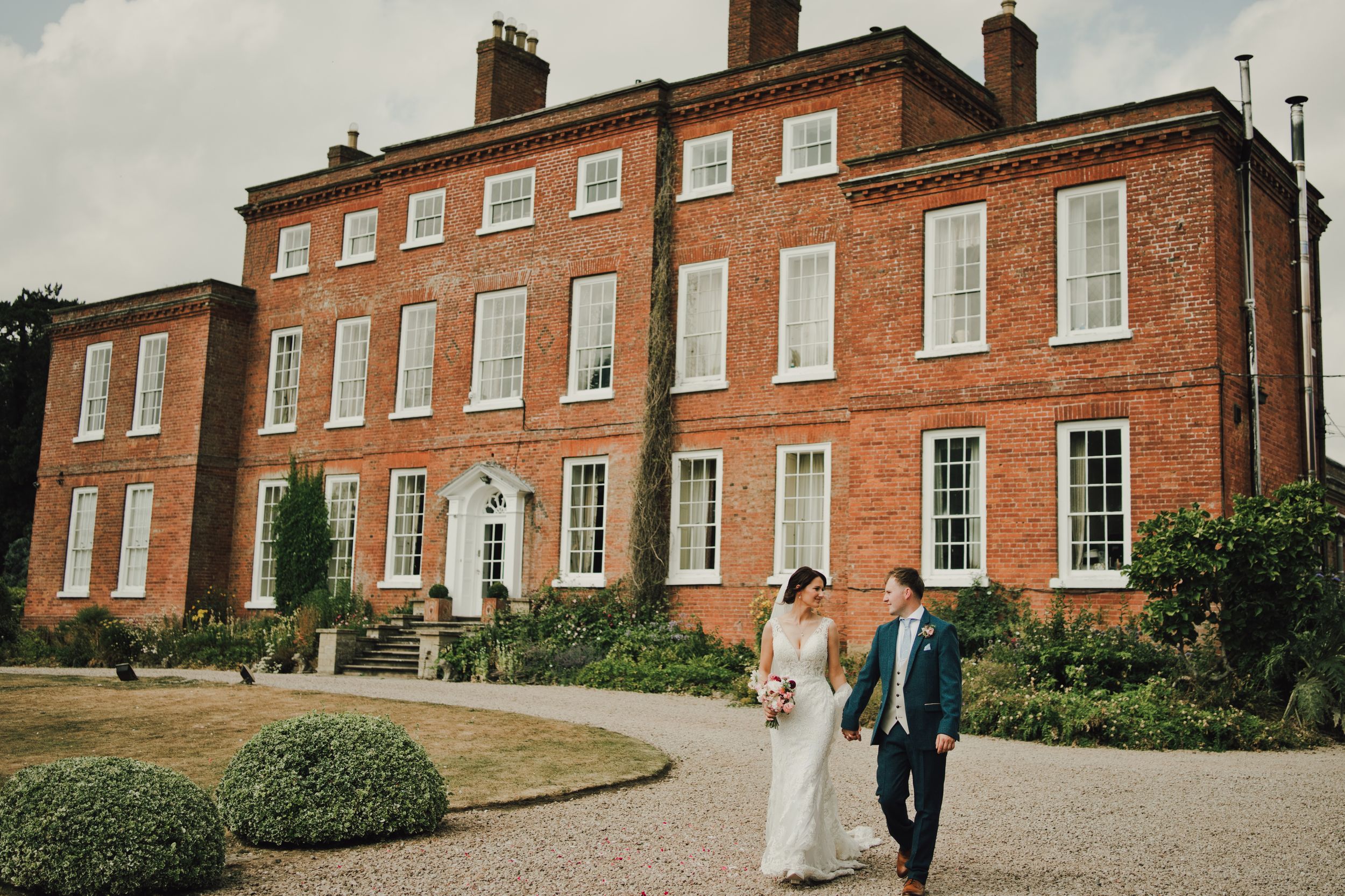 Bride and groom walking hand in hand outside a grand red brick Georgian wedding venue.