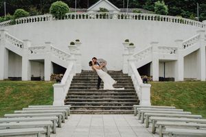 Grand white architectural staircase with symmetrical balustrades and columns at an outdoor wedding venue surrounded by greenery.