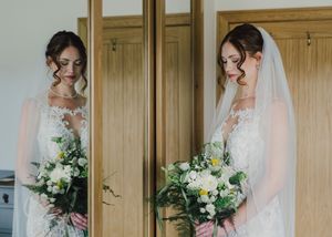 A bride in an elegant white wedding dress holds a beautiful bouquet of white and green flowers against wooden doors.