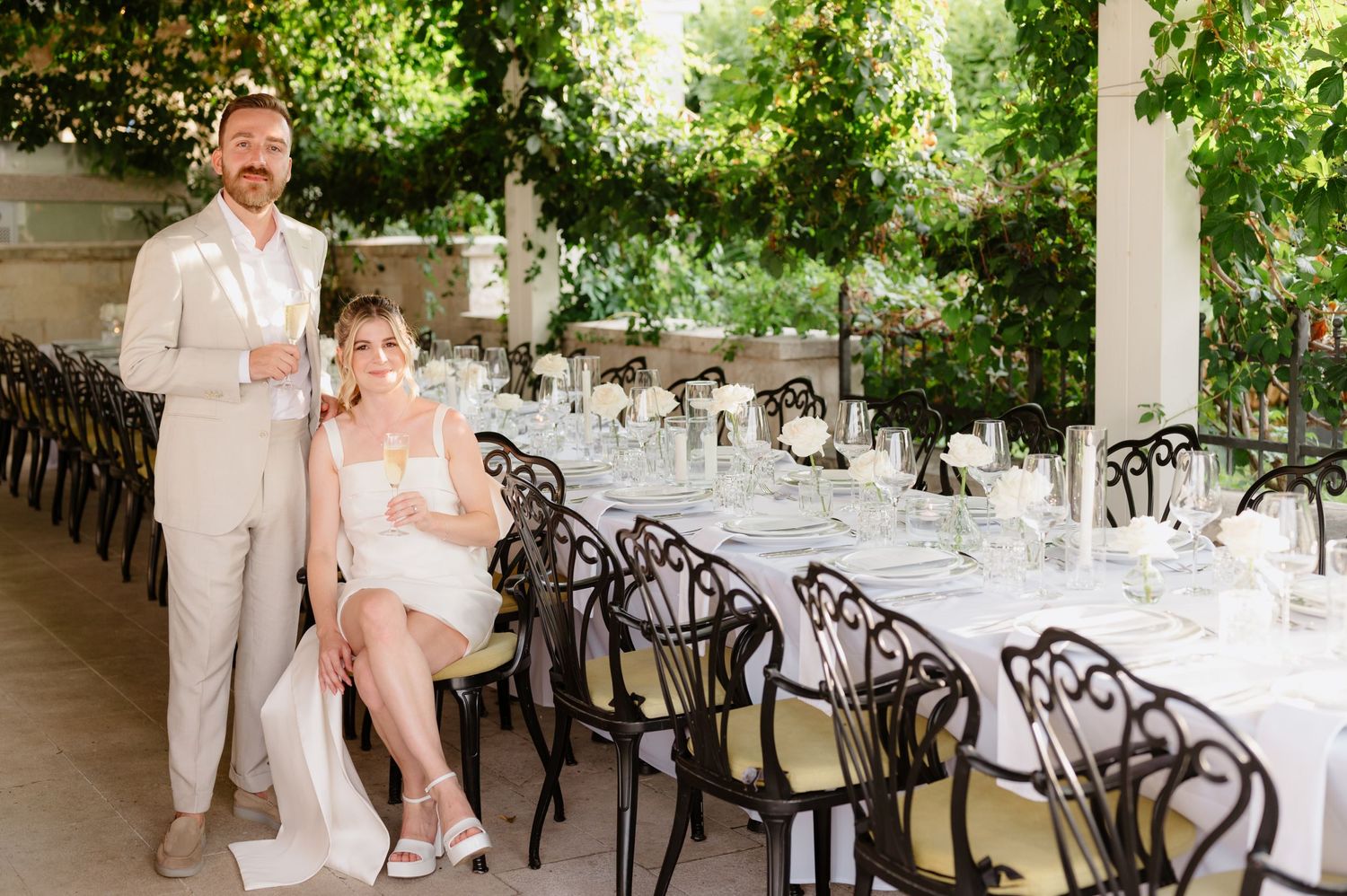 Wedding reception venue with elegant black chairs and white table settings under a covered terrace.